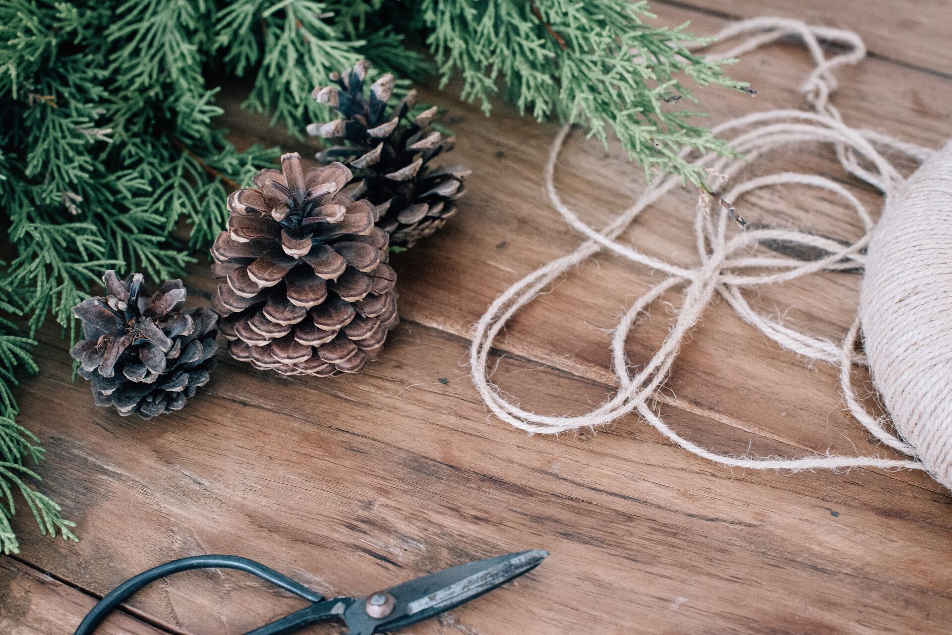 Scissors, twine, and pine cones on wooden table.